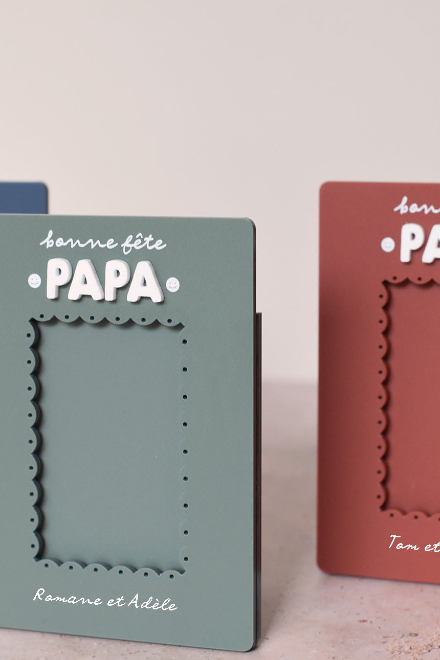 Cadre en plexi, format rectangulaire colors 3 coloris et texte blanc. Découpe de l’ouverture au centre en feston
Inscription en haut centré sur 2 lignes, ligne 1 « bonne fête », ligne 2 « Papa » en relief plexi blanc et sur les côtés du mot 2 smileys imprimés
Inscription en bas de deux prénoms
Zoom sur le cadre vert et le relief du mot « papa »