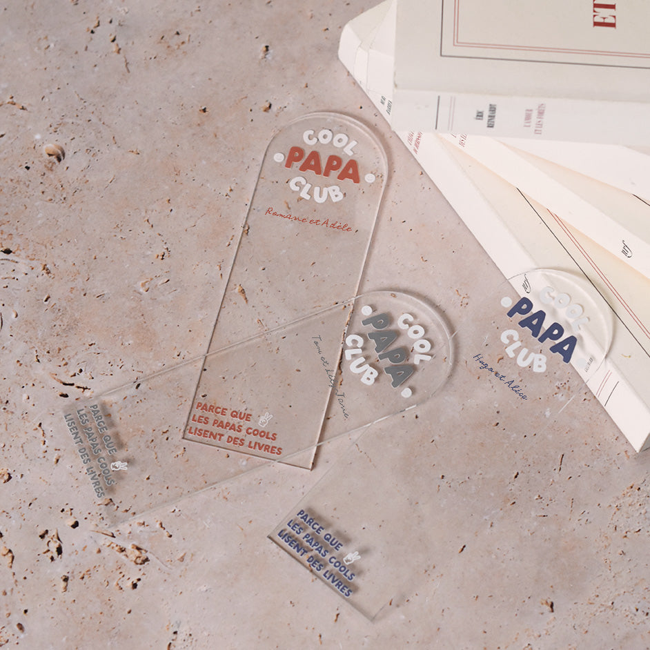 Marque-pages en plexi transparent découpe forme arche, texte blanc et coloré (3 options). Un modèle texte rouge terracotta et blanc, un modèle texte bleu et blanc et un modèle texte vert et blanc.
Inscription dans l’arche sur 3 lignes « Cool Papa Club », 2 smiley entourent le mot « PAPA ».
En dessous est inscrit un prénoms (personnalisation du produit)
En bas du marque-page est inscrit « Parque les papas cools lisent des livres » disposé sur 3 lignes avec un dessin de main en « v »