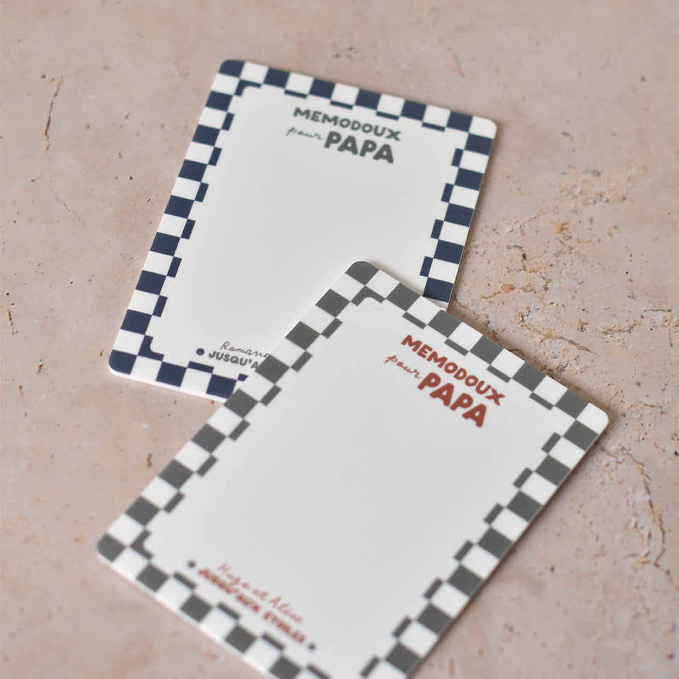 2 ardoises effaçable en plexiglass blanc avec un cadre à motif damier, inscription centrée en haut « memodoux pour papa » couleur rouge terracotta, inscription centré en bas de deux prénoms et en dessous « jusqu’au étoiles » avec deux smileys sur les côtés
2 modèles présentés : un modèle cadre damier bleu et texte vert, un modèle cadre damier vert et texte rouge terracotta