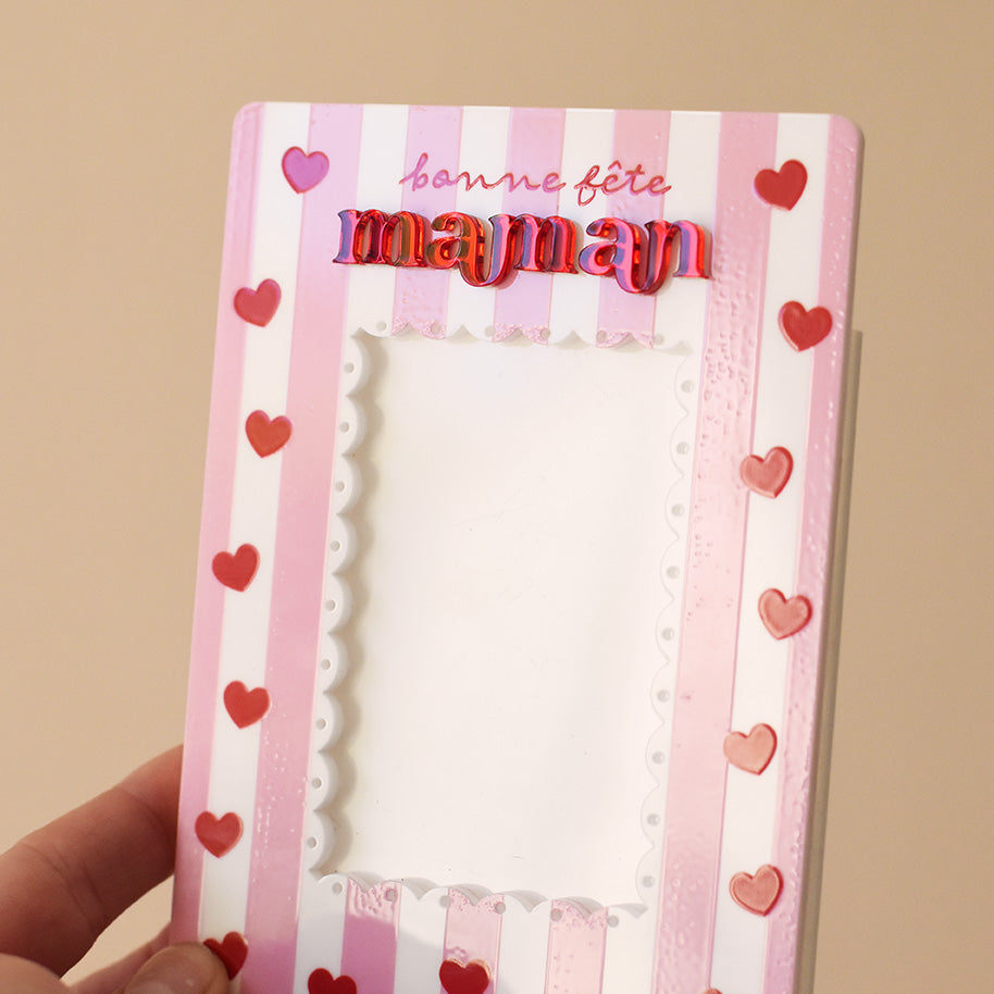 Cadre en plexiglass blanc imprimé
Illustrations rayures roses verticales et coeurs rouges
Inscription « bonne fête maman » - mot en « maman » en relief plexi miroir rouge
Format portrait rectangulaire
Centre du cadre (ouverture sur photo) découpe en feston