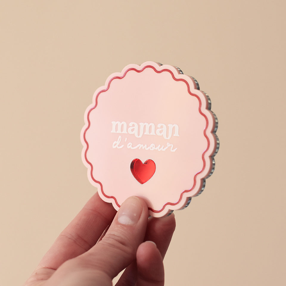 Miroir de poche forme rond festonné avec impression contour, inscription « maman d’amour » et coeur en plexi miroir incrusté au centre. Coloris face rose et rouge : fond plexi rose, contour rouge, texte blanc, coeur en plexi miroir rouge