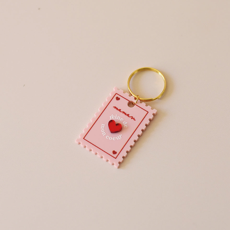 Porte-clés plexi coloré rose et rouge, design de carte à jour, forme de timbre et coeur au centre en relief, anneau doré. Inscription reine de mon coeur