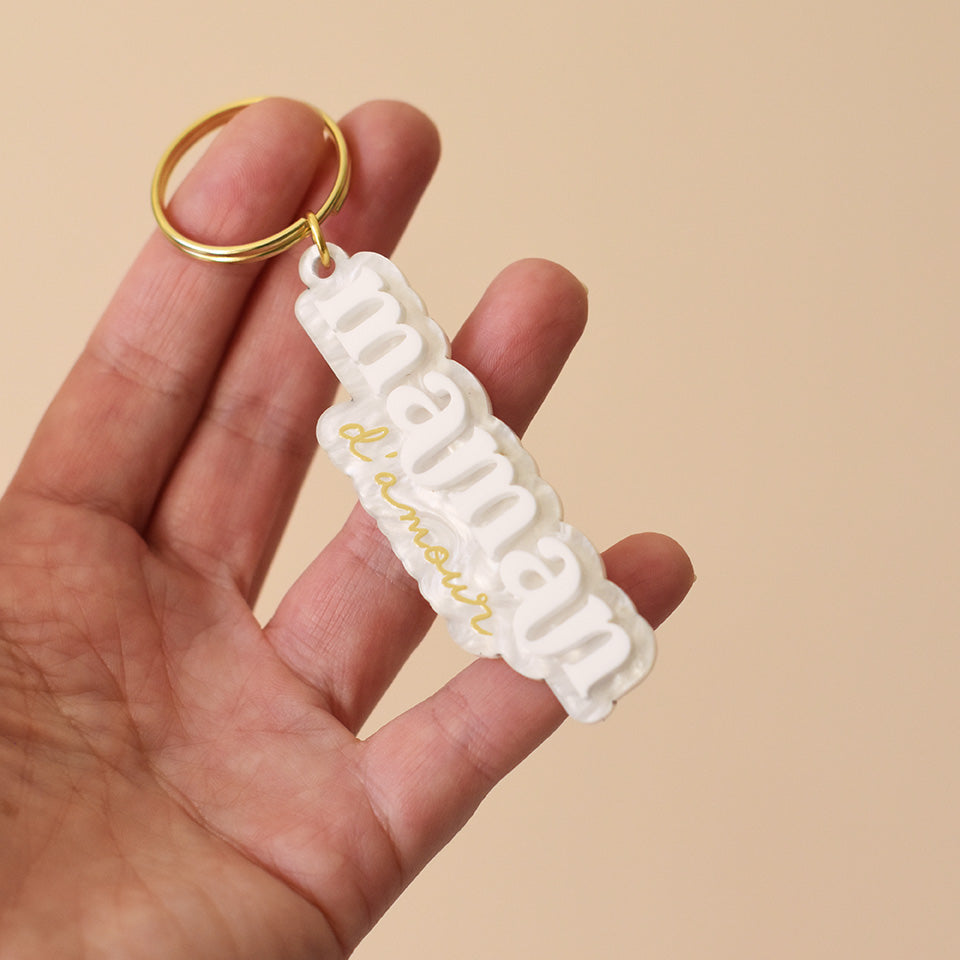 Porte-clés plexi coloré fond marbré blanc inscription « maman d’amour », « maman » en relief blanc et « d’amour » imprimé en doré, découpe à la forme du lettrage sur anneau doré