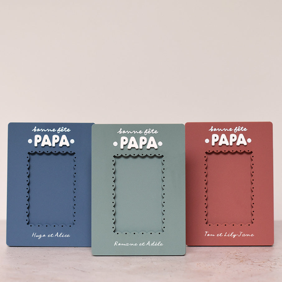 3 cadres en plexi, format rectangulaire coloris uni et texte blanc. Découpe de l’ouverture au centre en feston 
Inscription en haut centré sur 2 lignes, ligne 1 « bonne fête », ligne 2 « Papa » en relief plexi blanc et sur les côtés du mot 2 smileys imprimés
Inscription en bas de deux prénoms 
3 modèles : un modèle bleu, un modèle vert et un modèle rouge terracotta
