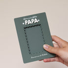 Cadre en plexi, format rectangulaire colors vert « pin » et texte blanc. Découpe de l’ouverture au centre en feston 
Inscription en haut centré sur 2 lignes, ligne 1 « bonne fête », ligne 2 « Papa » en relief plexi blanc et sur les côtés du mot 2 smileys imprimés
Inscription en bas de deux prénoms