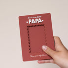 Cadre en plexi, format rectangulaire colors rouge « terrcotta » et texte blanc. Découpe de l’ouverture au centre en feston 
Inscription en haut centré sur 2 lignes, ligne 1 « bonne fête », ligne 2 « Papa » en relief plexi blanc et sur les côtés du mot 2 smileys imprimés
Inscription en bas de deux prénoms
