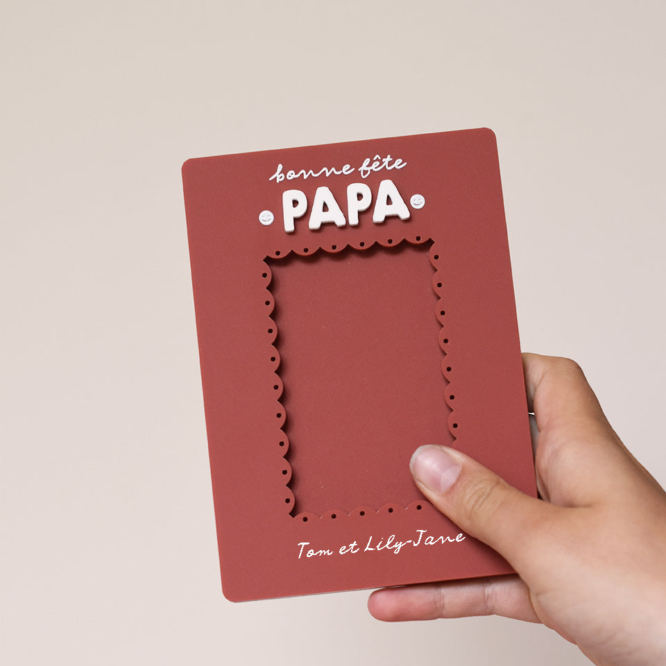 Cadre en plexi, format rectangulaire colors rouge « terrcotta » et texte blanc. Découpe de l’ouverture au centre en feston 
Inscription en haut centré sur 2 lignes, ligne 1 « bonne fête », ligne 2 « Papa » en relief plexi blanc et sur les côtés du mot 2 smileys imprimés
Inscription en bas de deux prénoms
