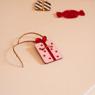 Découpes de plexi coloré avec impression de détails
Il y a 2 trous par découpes et une cordelette est passée dedans
Illustration d’un cadeau rose à pois et noeud rouges
 