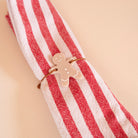 Découpes de plexi couleur beige avec impression de détails blanc
Il y a 2 trous par découpes et une cordelette est passée dedans
La découpe représente un bonhomme en pain d’épice
Il est accroché sur une serviette à rayures blanches et rouges
 