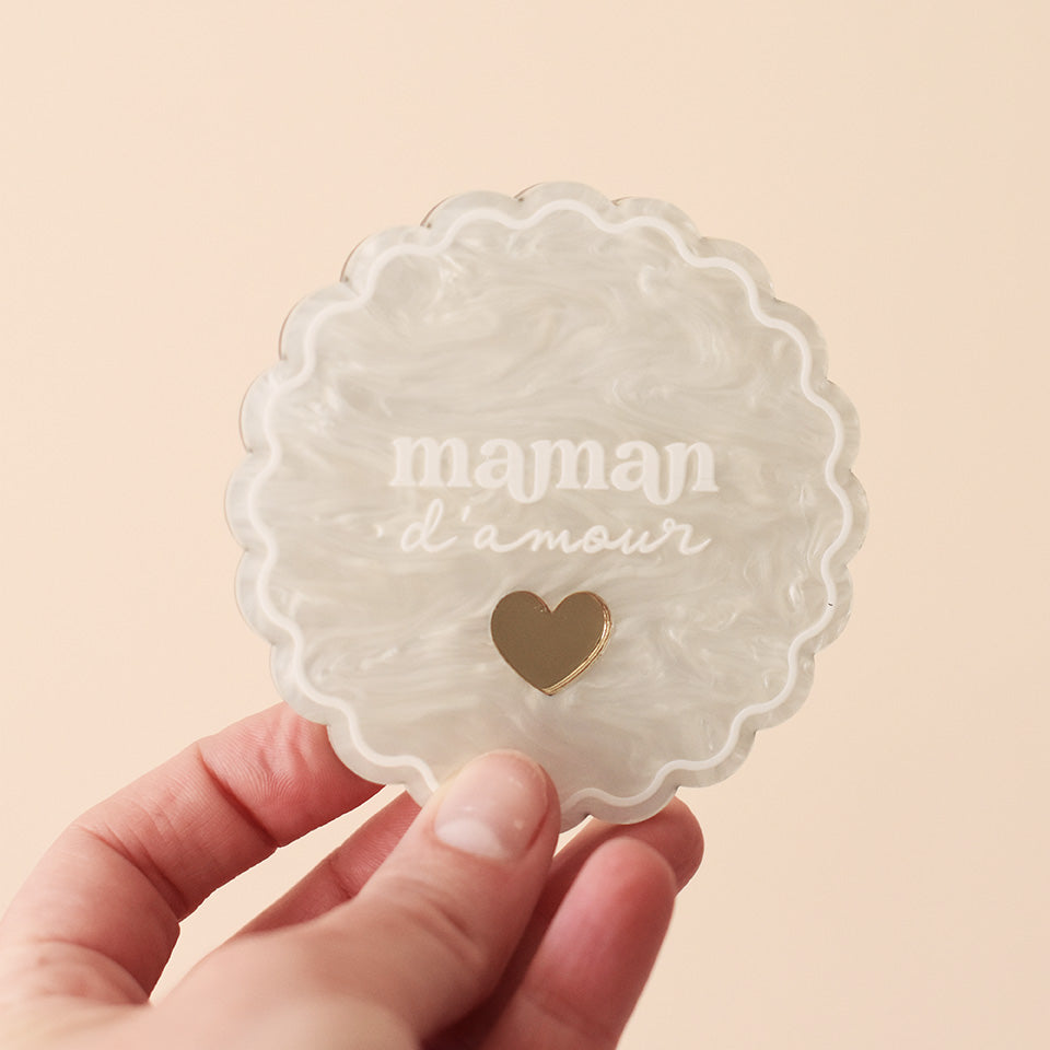 Miroir de poche forme rond festonné avec impression contour, inscription « maman d’amour » et coeur en plexi miroir incrusté au centre. Coloris face marbré blanc : fond plexi marbré blanc, contour et teste blanc, coeur en plexi miroir or 