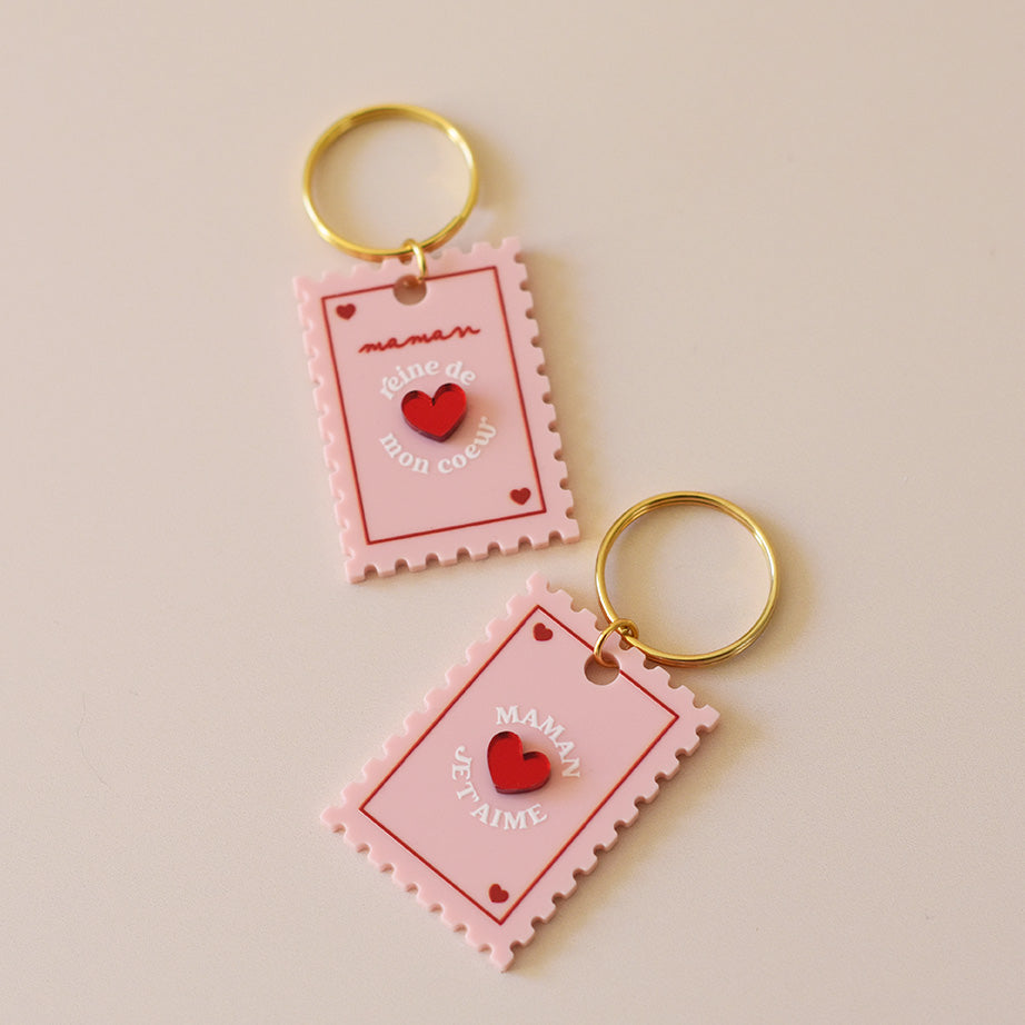Porte-clés plexi coloré rose et rouge, design de carte à jour, forme de timbre et coeur au centre en relief, anneau doré.  Inscription maman je t’aime ou reine de mon coeur 
