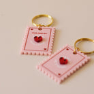 Porte-clés plexi coloré rose et rouge, design de carte à jour, forme de timbre et coeur au centre en relief, anneau doré.  Inscription maman je t’aime ou reine de mon coeur - focus relief 
