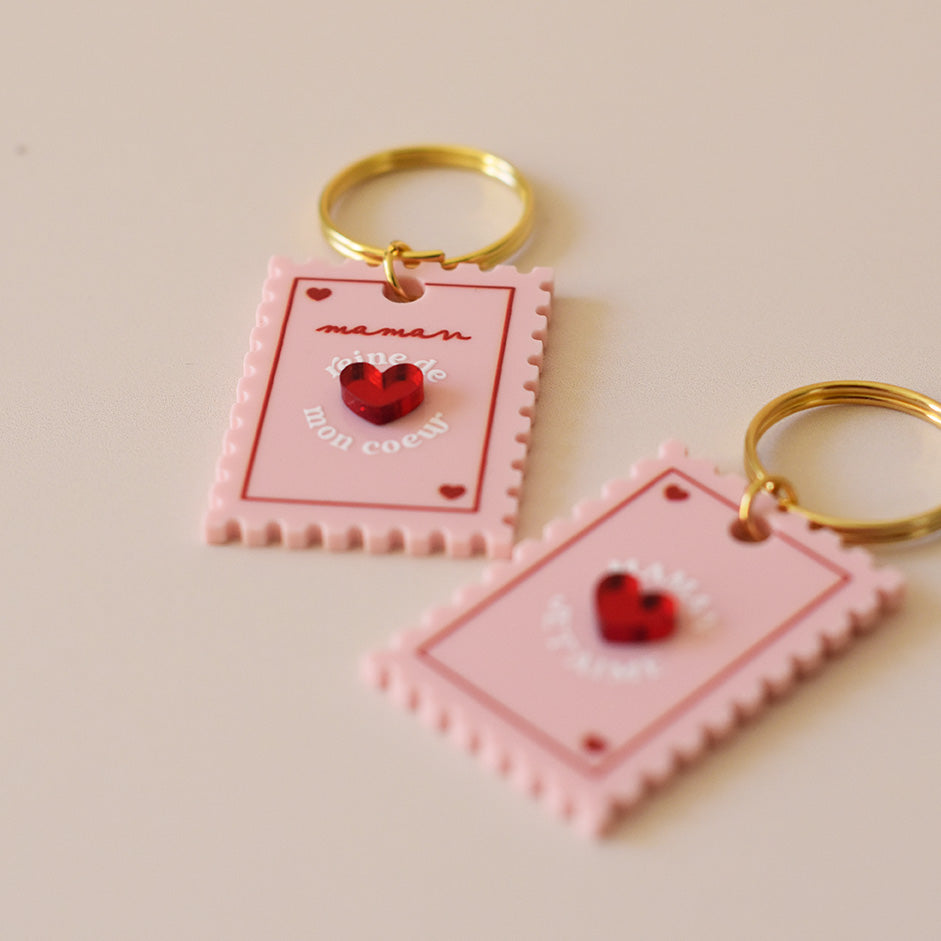 Porte-clés plexi coloré rose et rouge, design de carte à jour, forme de timbre et coeur au centre en relief, anneau doré.  Inscription maman je t’aime ou reine de mon coeur - focus relief 