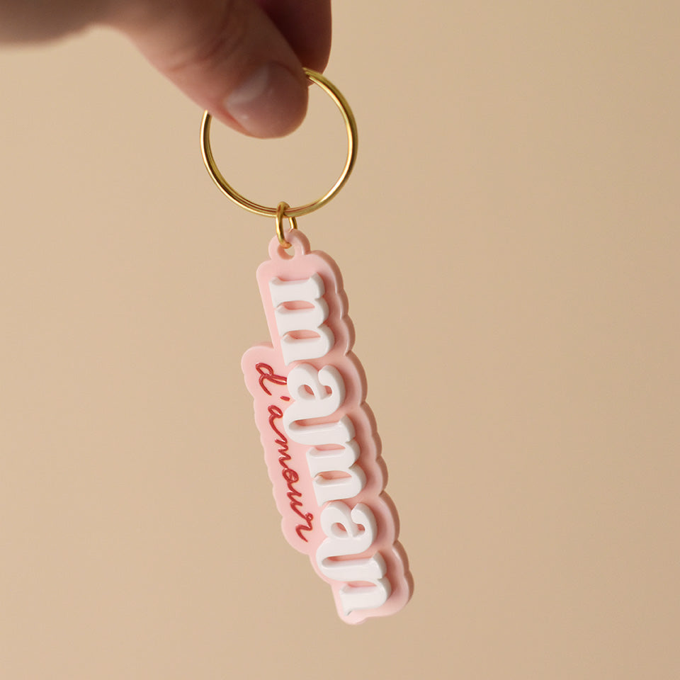 Porte-clés plexi coloré fond rose inscription « maman d’amour », « maman » en relief blanc et « d’amour » imprimé en rouge découpe à la forme du lettrage sur anneau doré